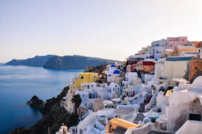 Numerous white buildings sitting on the side of a mountain overlooking the sea in Santorini, Greece