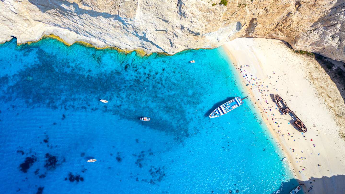 An bird's eye view of a boat in the water next to the sand at Navagio Beach, Zakynthos, Greece