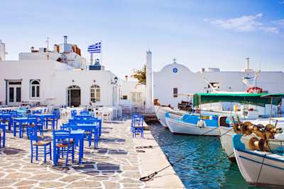 Blue chairs and tables outside a cafe by docked boats at the harbour on a sunny day, Naoussa, Paros, Greece