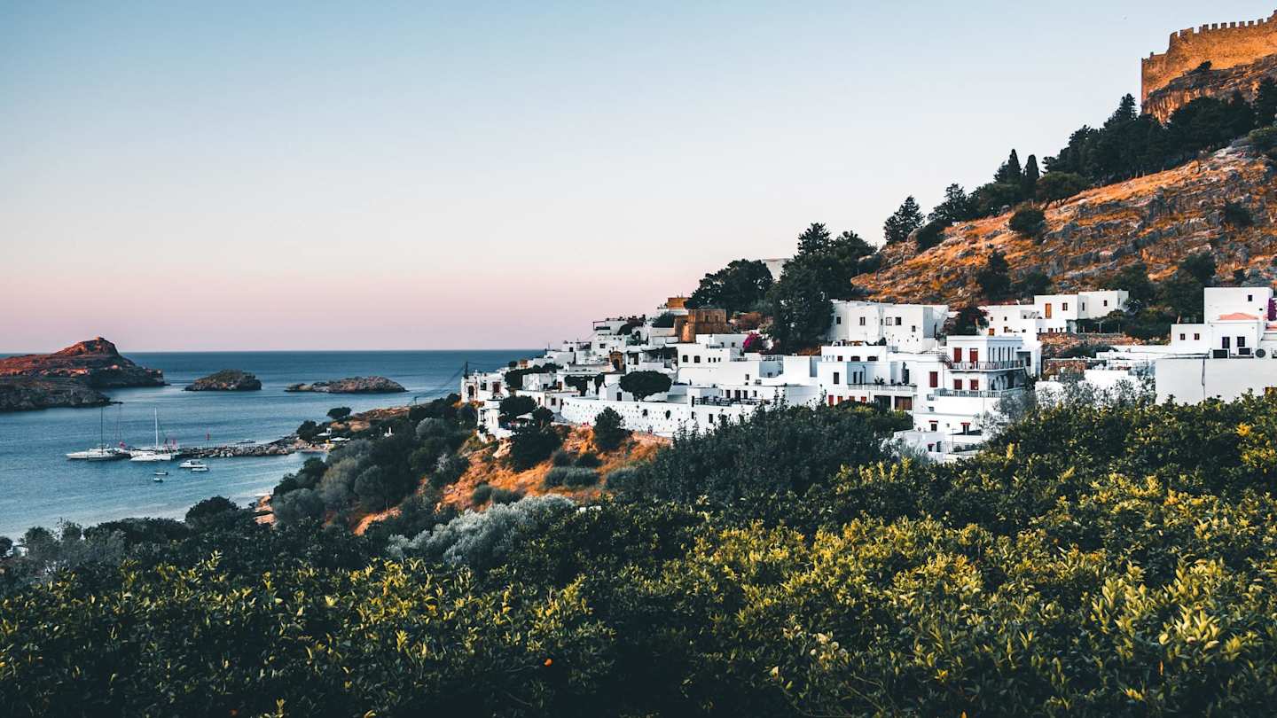 A view over the coastline with white buildings clustered on the side of a tall hill, Rhodes, Greece