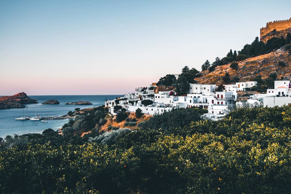 A view over the coastline with white buildings clustered on the side of a tall hill, Rhodes, Greece