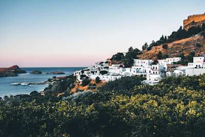 A view over the coastline with white buildings clustered on the side of a tall hill, Rhodes, Greece