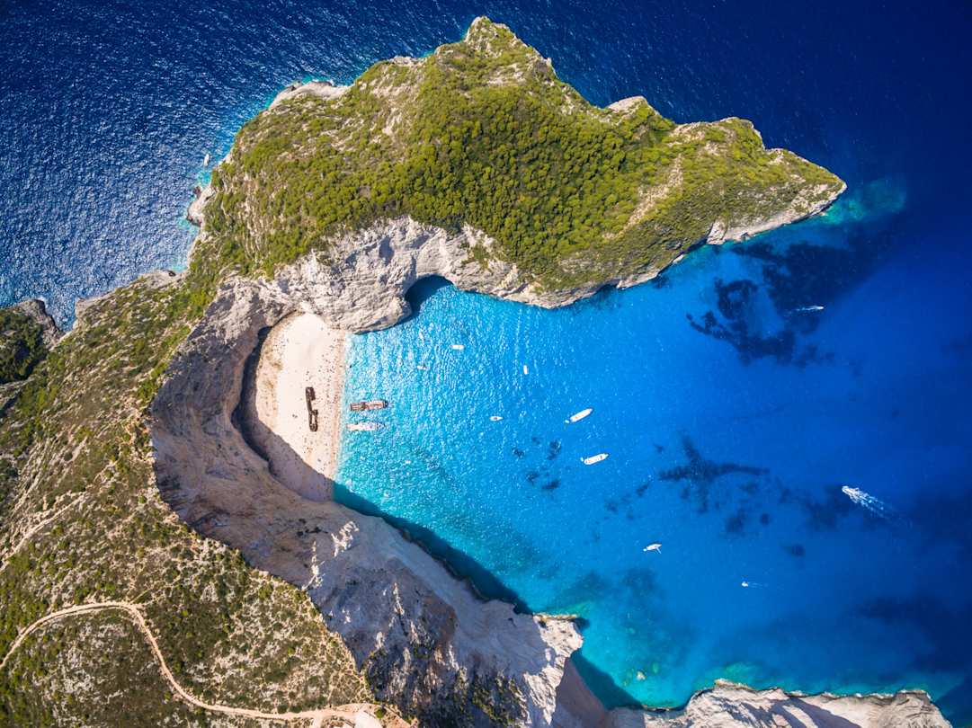 A bird's eye view of the shipwreck on Navagio Beach by the clear blue sea and grassy cliffs, Zakynthos, Greece