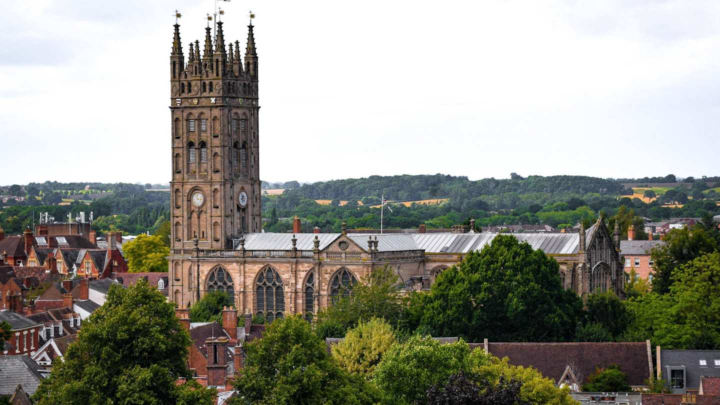 A view of Warwick castle over houses and green trees from a distance, Warwickshire, England, UK