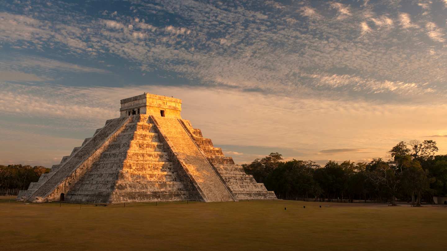 A view of the El Castillo pyramid in front of green trees at sunset, Chichén Itzá, Mexico