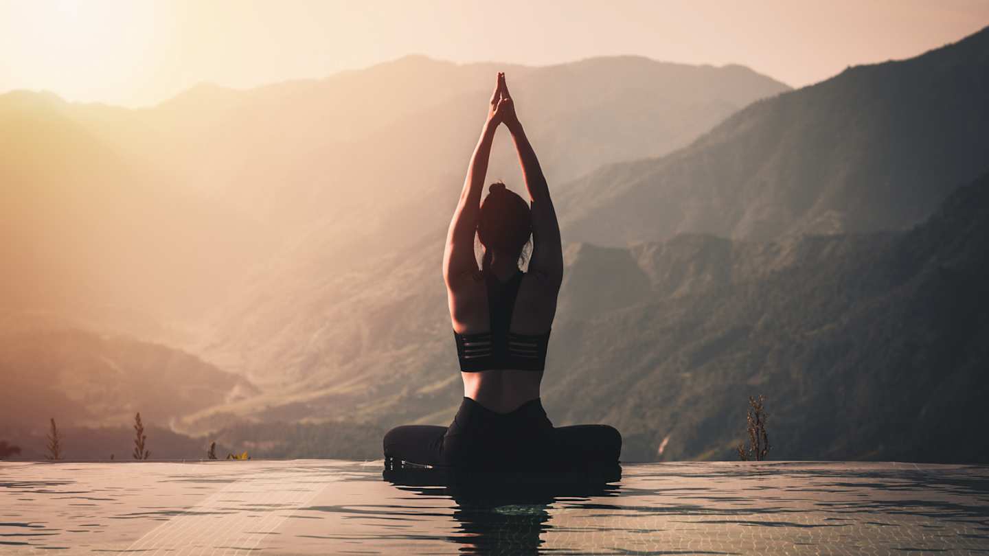 A woman doing yoga on the edge of a pool overlooking mountains at sunrise