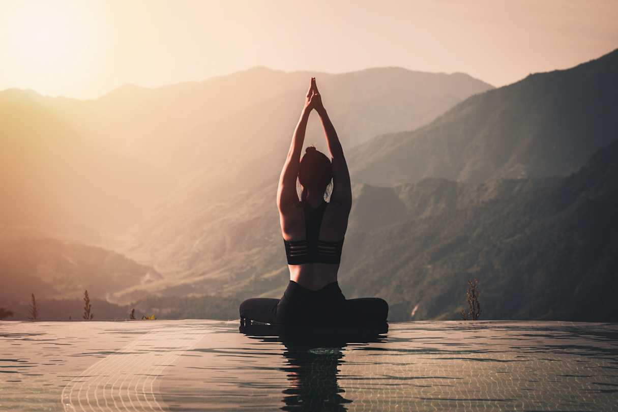 A woman doing yoga on the edge of a pool overlooking mountains at sunrise