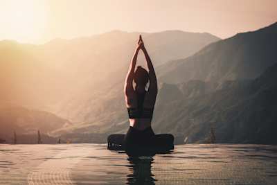 A woman doing yoga on the edge of a pool overlooking mountains at sunrise