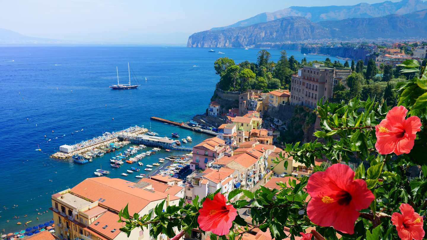 Landscape view of red flowers, orange houses, and blue sea in Sorrento, Italy
