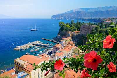 Landscape view of red flowers, orange houses, and blue sea in Sorrento, Italy