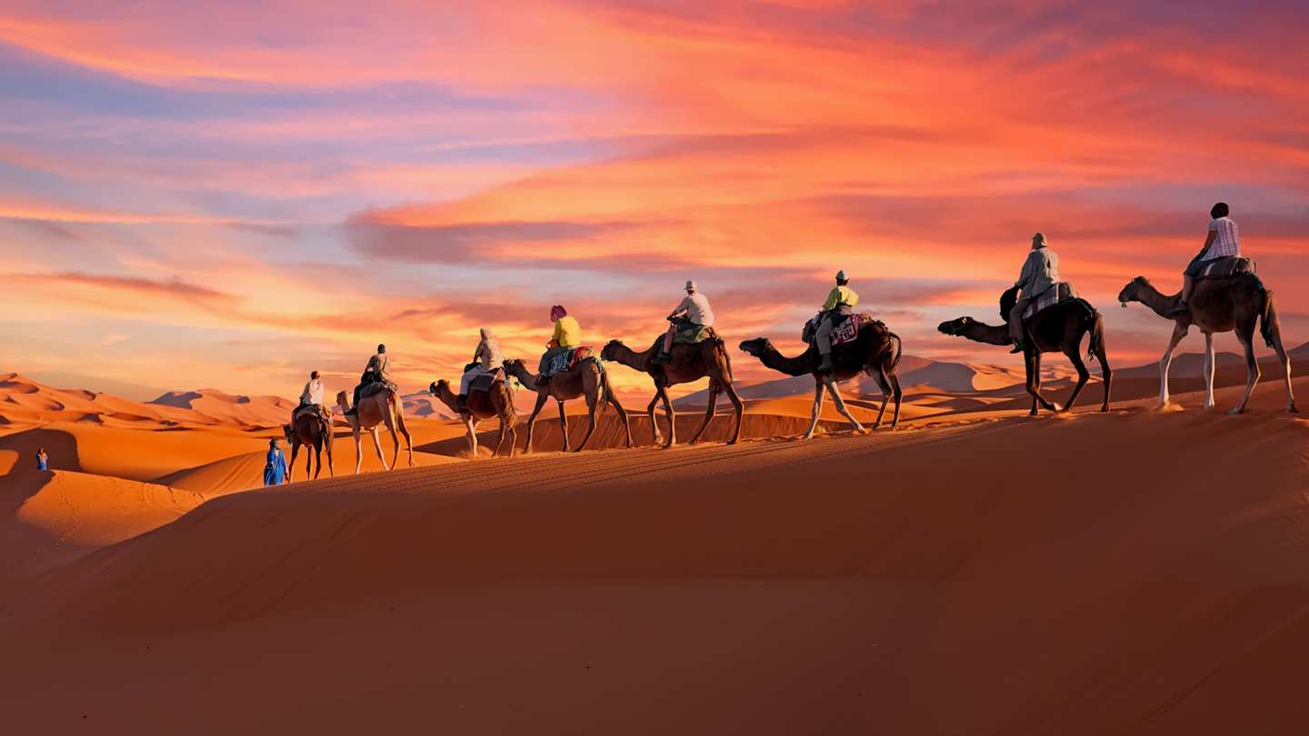 A group of people riding camels through the desert at sunset, Morocco