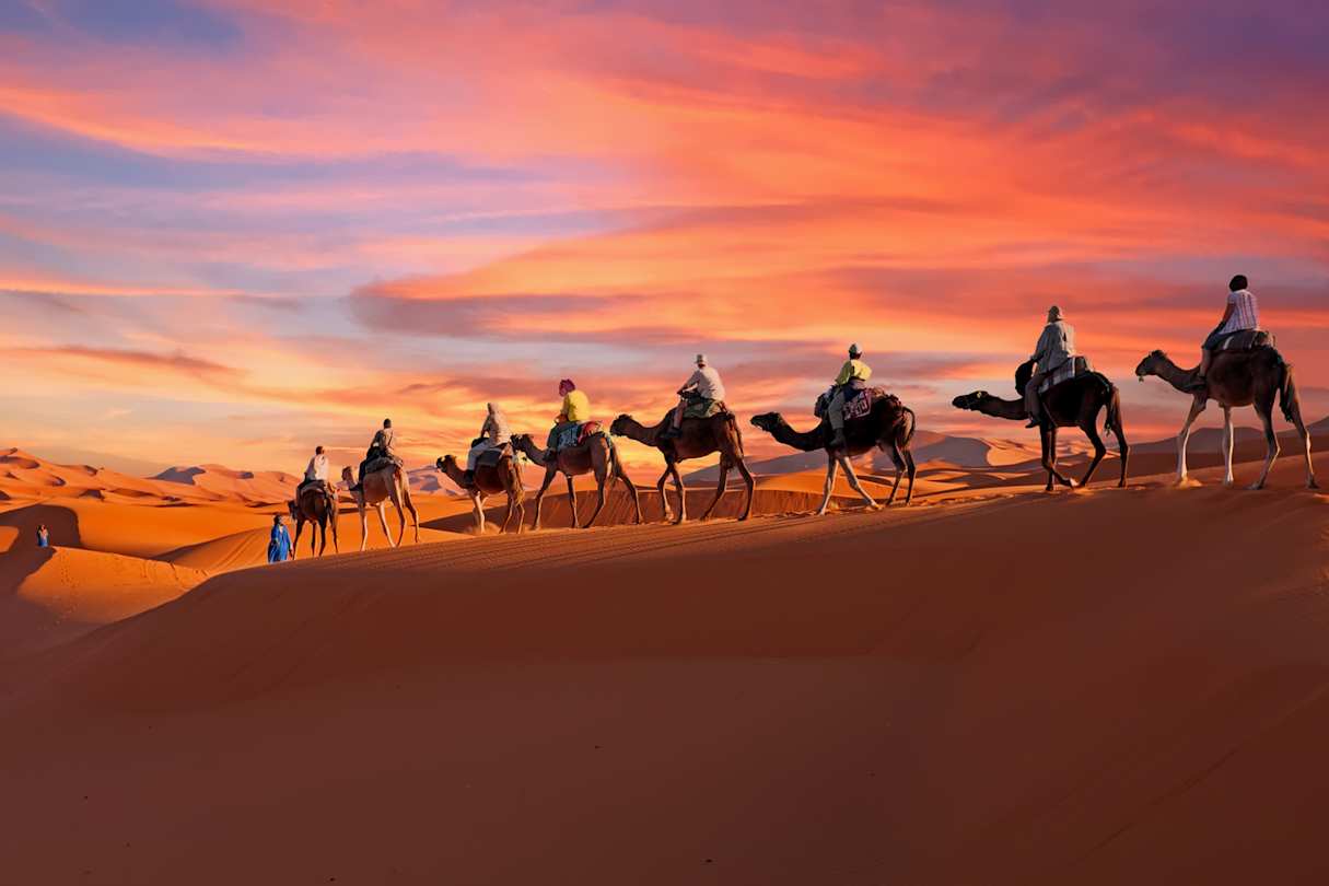 A group of people riding camels through the desert at sunset, Morocco