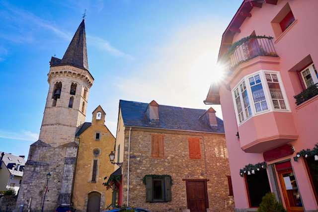 A pink building, stone house and the Church of Sant Miquèu captured on a sunny day in Veilha, near Baqueira-Beret