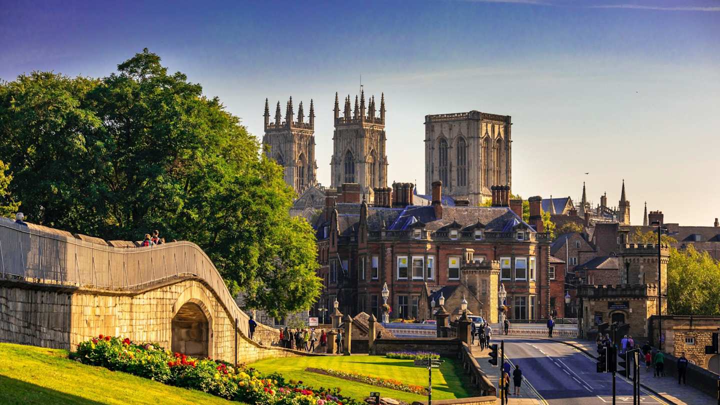 York Minster in the distance behind green trees and brown buildings, York, England, UK