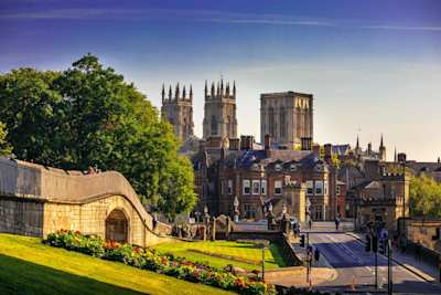 York Minster in the distance behind green trees and brown buildings, York, England, UK