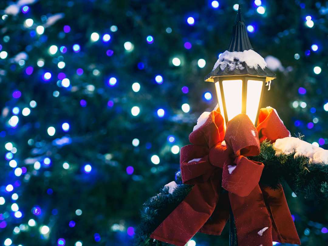 Lit, snow-covered lantern in front of a Christmas tree