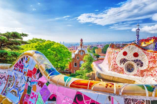 A colourful wall overlooking green trees and buildings in Park Guell, Barcelona, Spain
