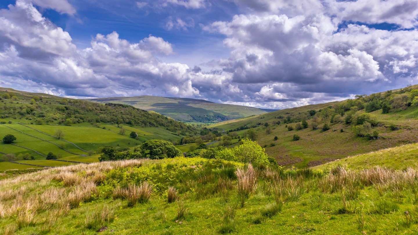 A view of large green meadows and hills on a sunny day in the Yorkshire Dales, England, UK