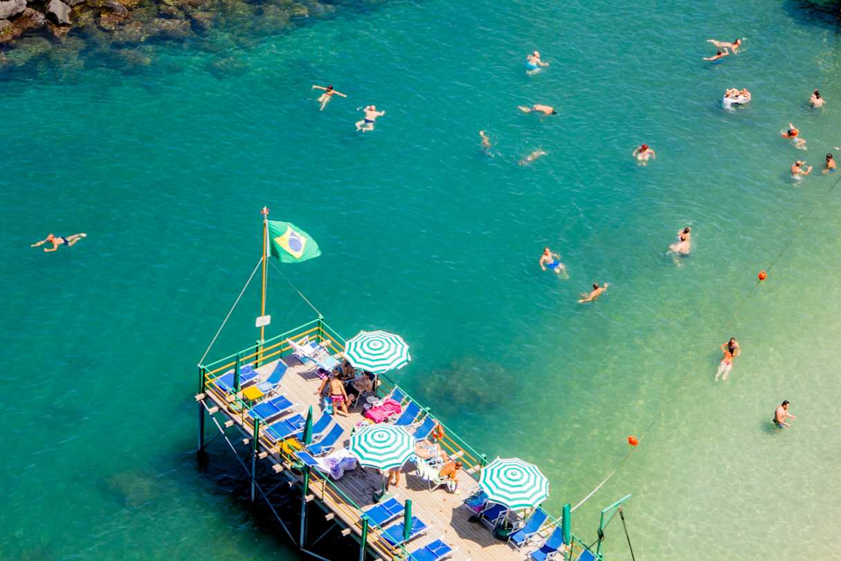 Tourists swimming in calm waters and relaxing on sun loungers at the beach in Sorrento, Italy