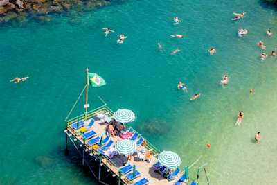 Tourists swimming in calm waters and relaxing on sun loungers at the beach in Sorrento, Italy