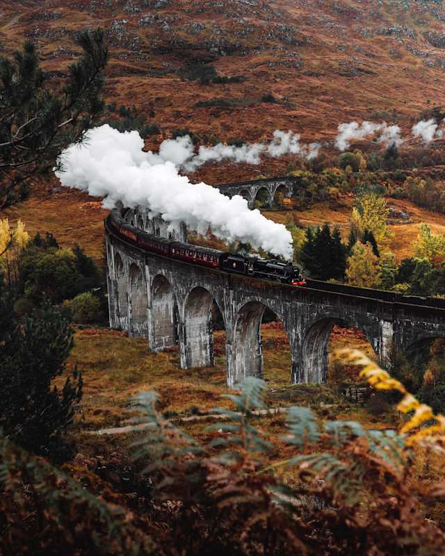 A black steam train on the Glenfinnan Viaduct in autumn, Scotland, UK