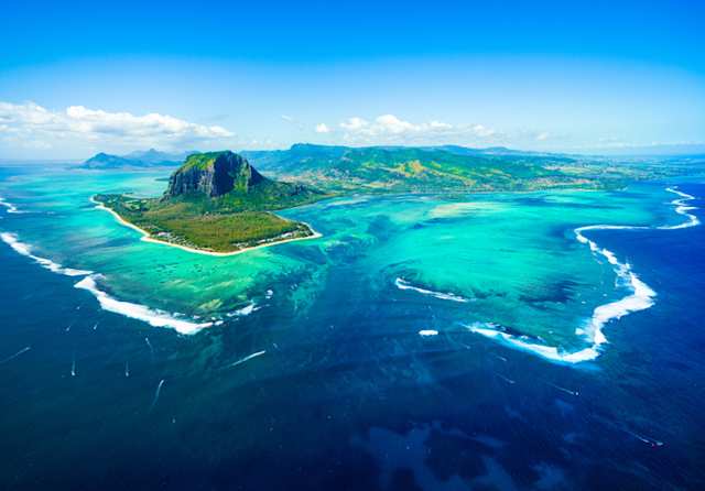 An aerial view of vast areas of blue sea by a large green island in Mauritius