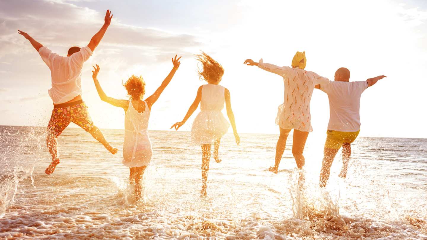 A family of parents and teenagers running into the sea at sunset