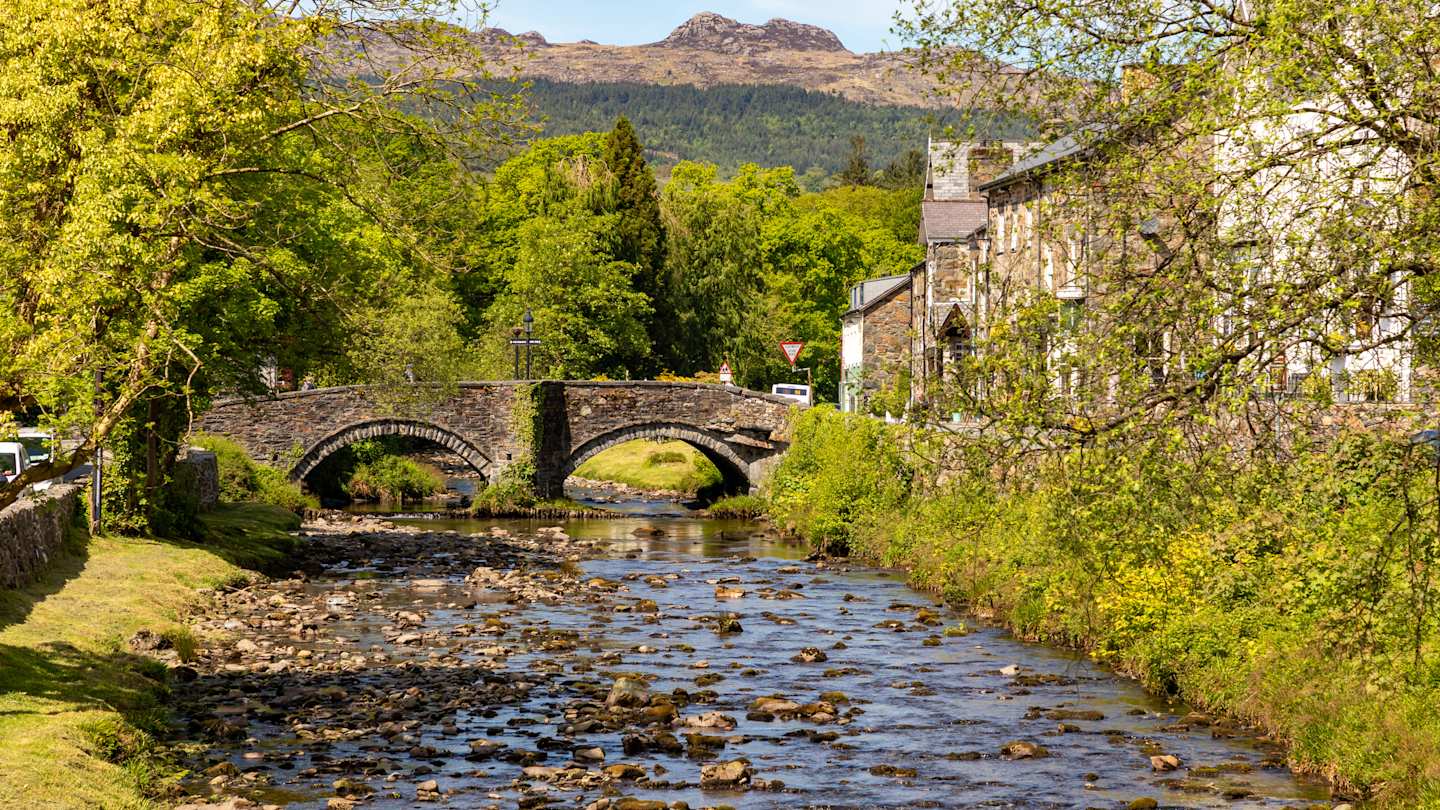 Attractive stone buildings and quaint bridge beside the River Glaslyn during autumn in Beddgelert, North Wales