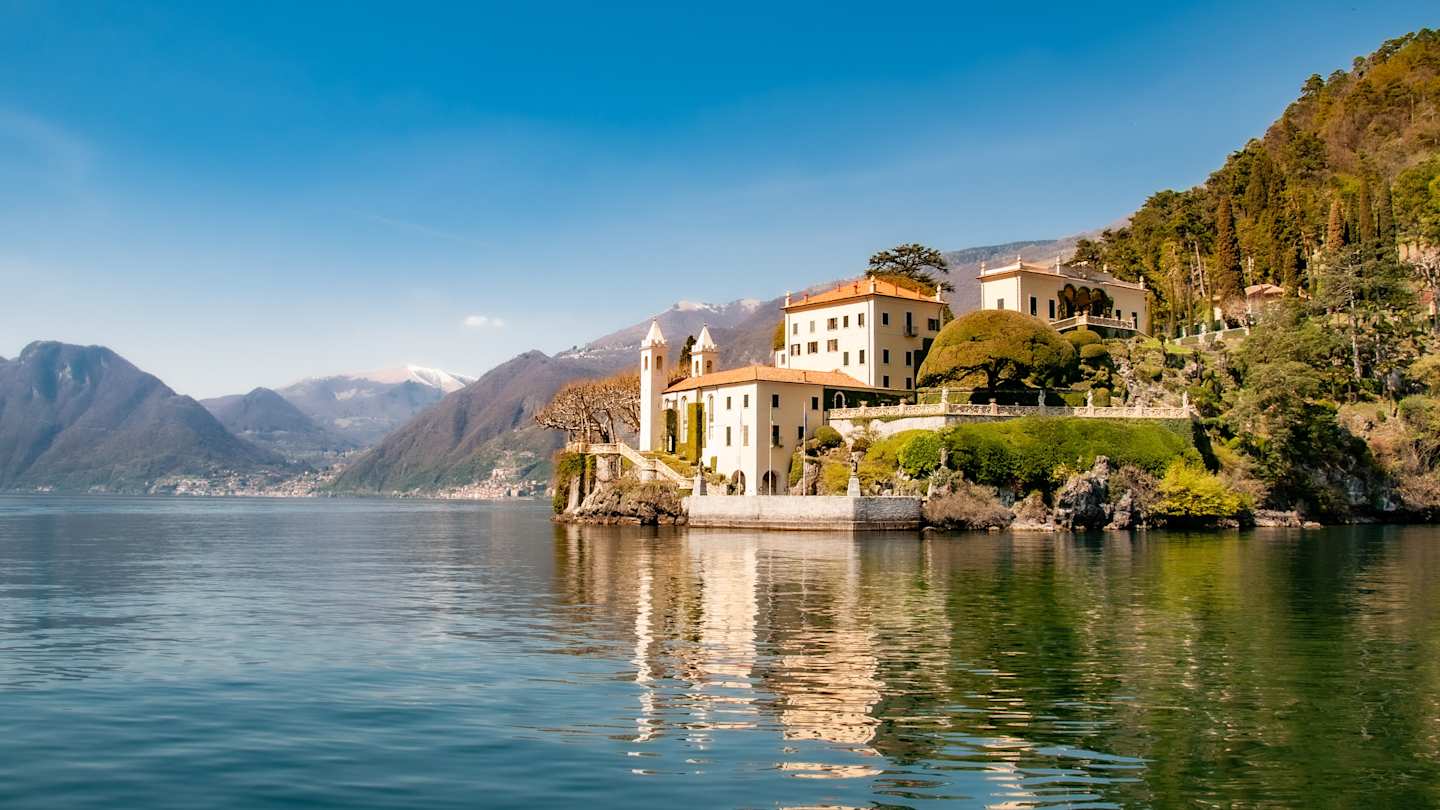 A large white building and hills next to Lake Como, Italy