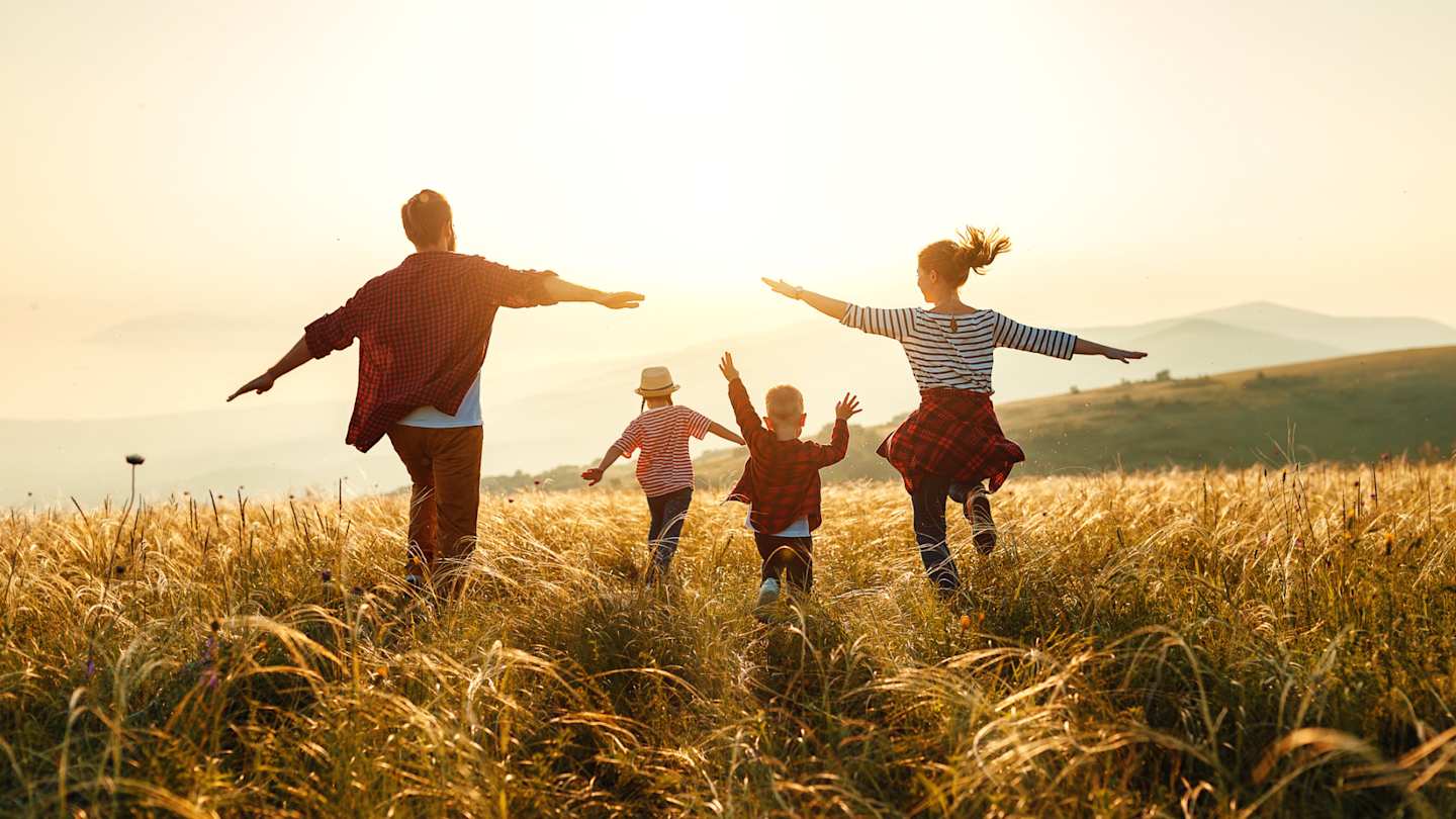 A young family running happily through a field on holiday at sunset