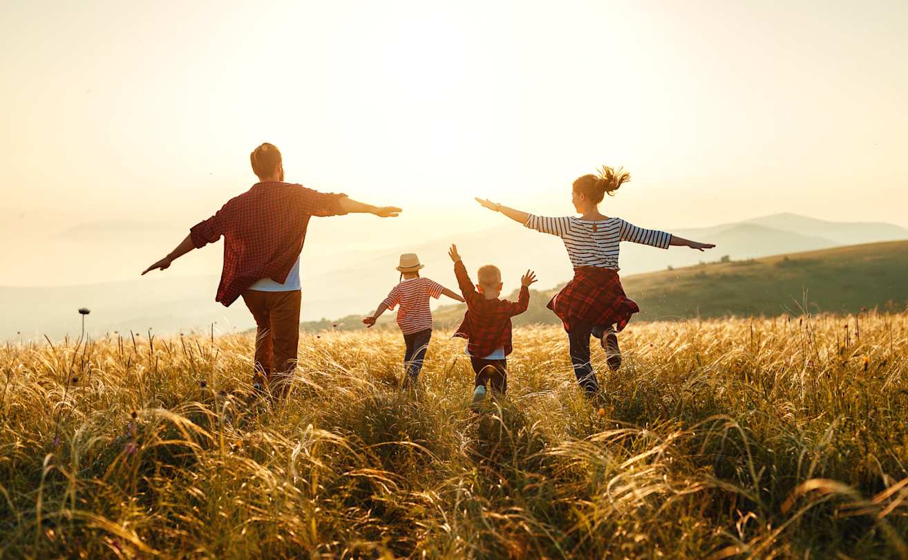 A young family running happily through a field on holiday at sunset