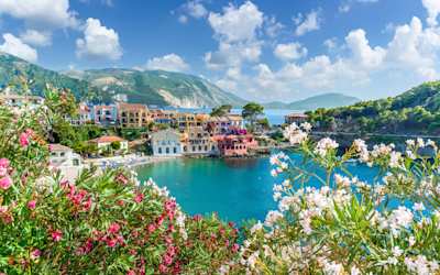 Colourful houses in Assos on the water, surrounded by pink and white flowers and mountains in the background, Kefalonia