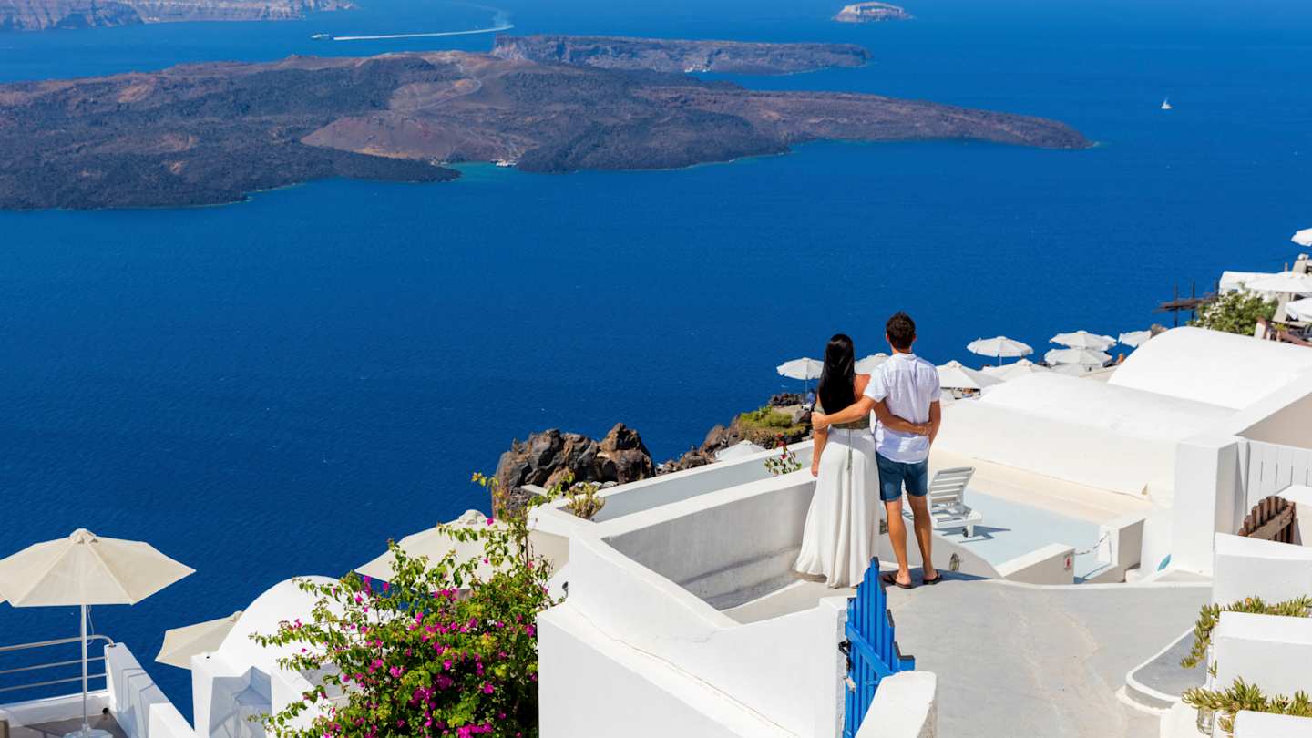 A young couple standing looking out to sea from a rooftop in Santorini, Greece