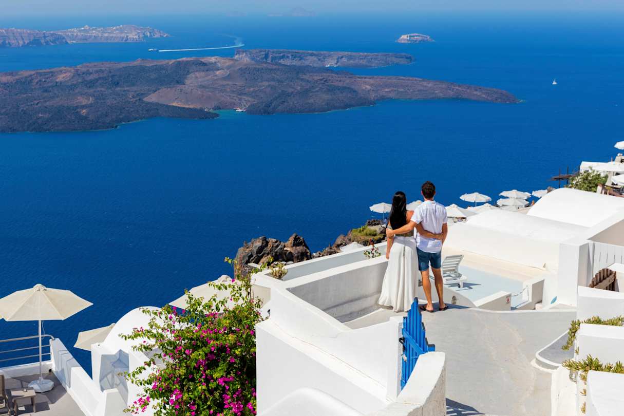 A young couple standing looking out to sea from a rooftop in Santorini, Greece