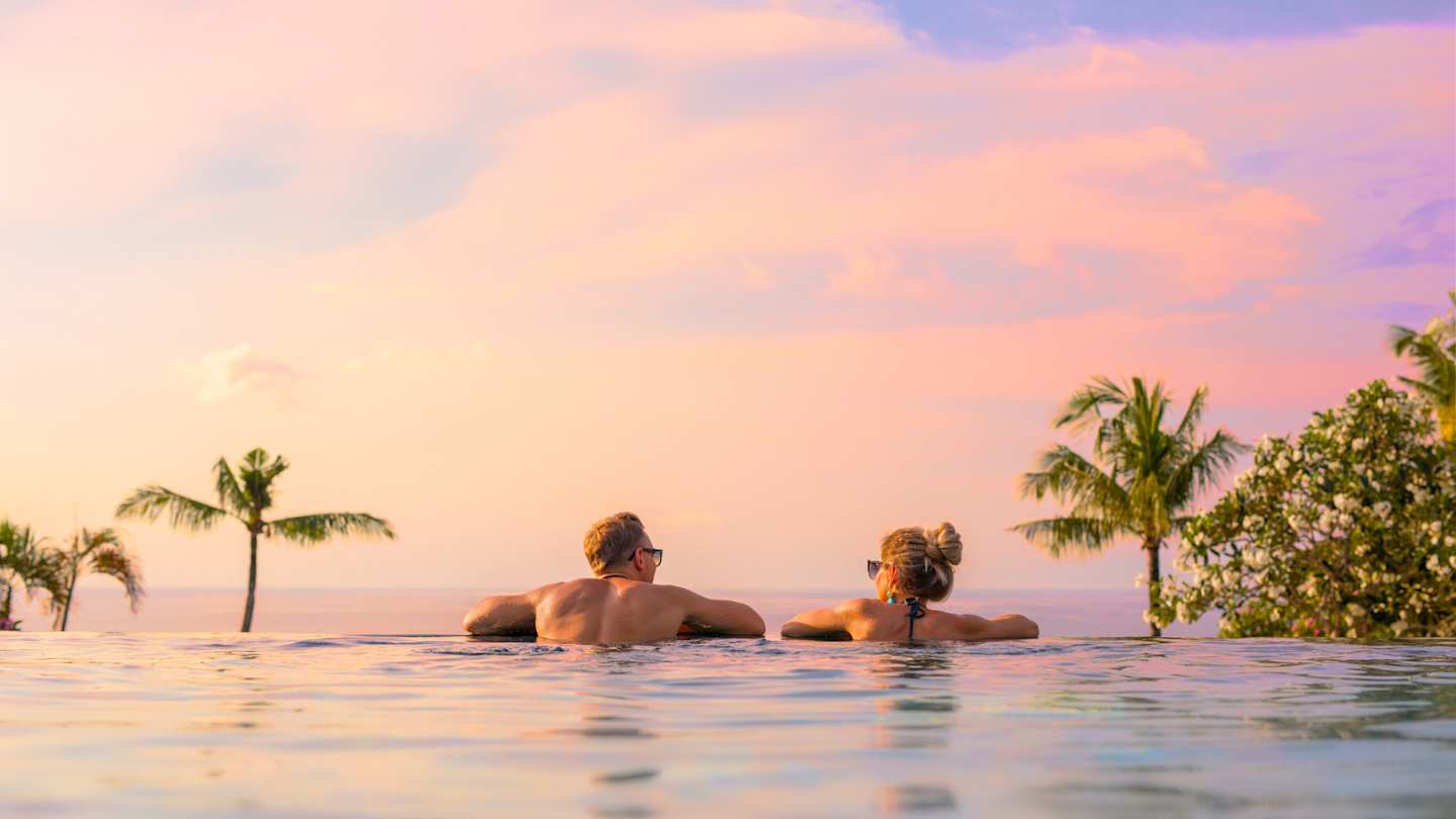 A view of a couple overlooking the sea in an infinity pool at sunset