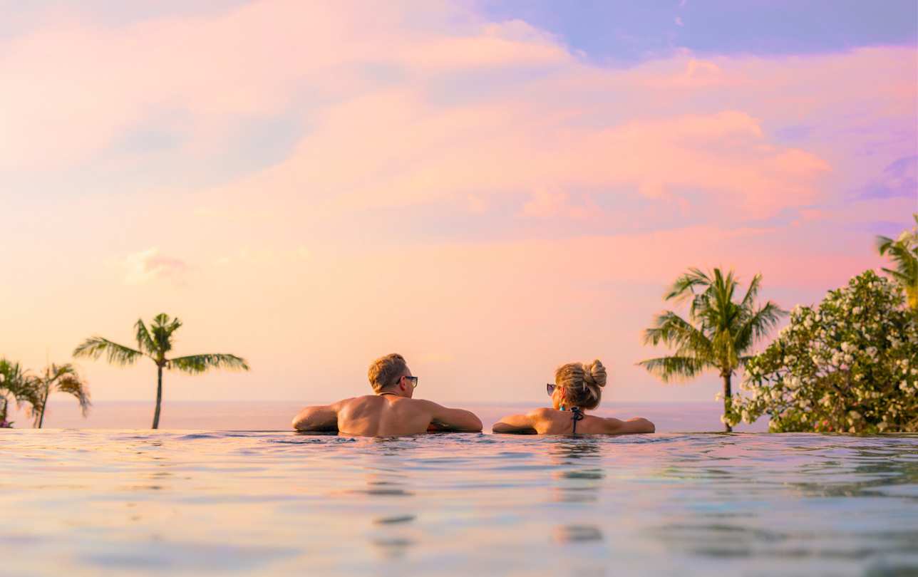 A view of a couple overlooking the sea in an infinity pool at sunset