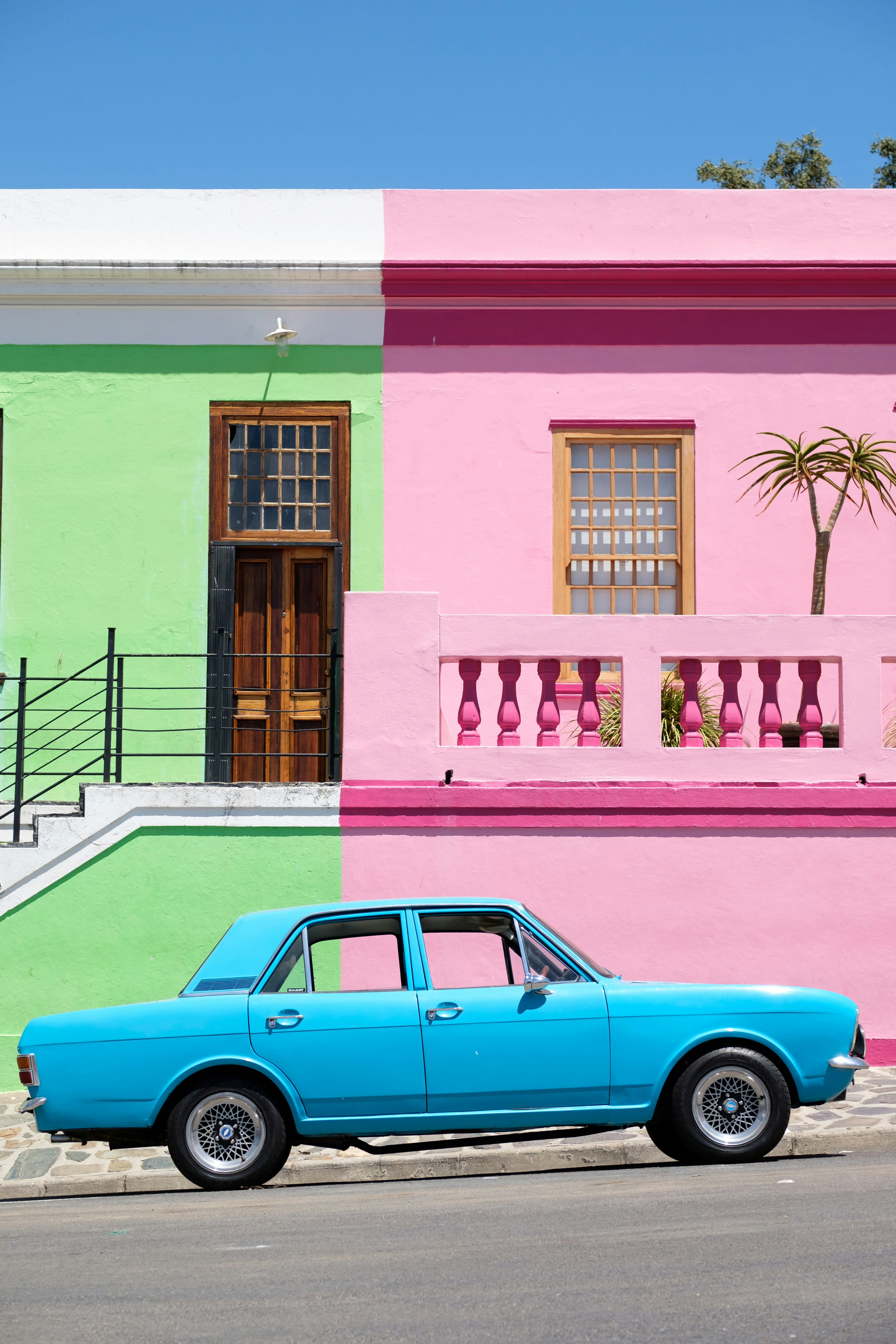 A colourful portrait of an old blue sedan vehicle in front of pink and green house in Bo-Kaap, Cape Town, South Africa