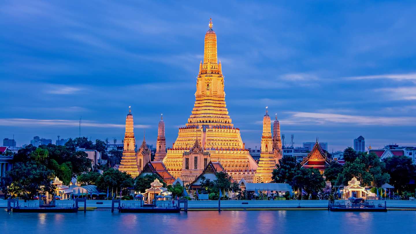 A view of the Wat Arun Temple behind a large river, lit up at night, Bangkok, Thailand