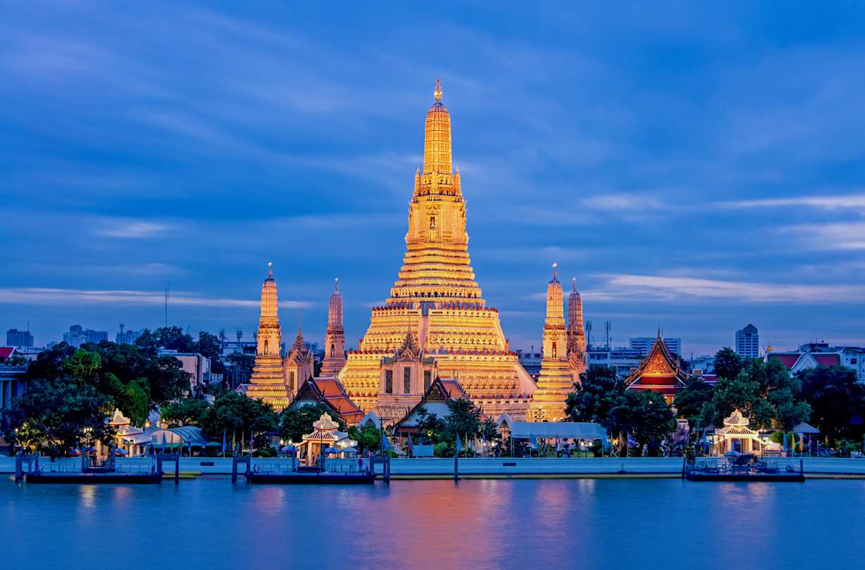 A view of the Wat Arun Temple behind a large river, lit up at night, Bangkok, Thailand
