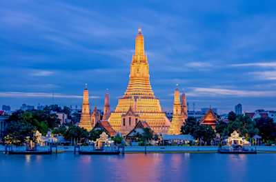 A view of the Wat Arun Temple behind a large river, lit up at night, Bangkok, Thailand