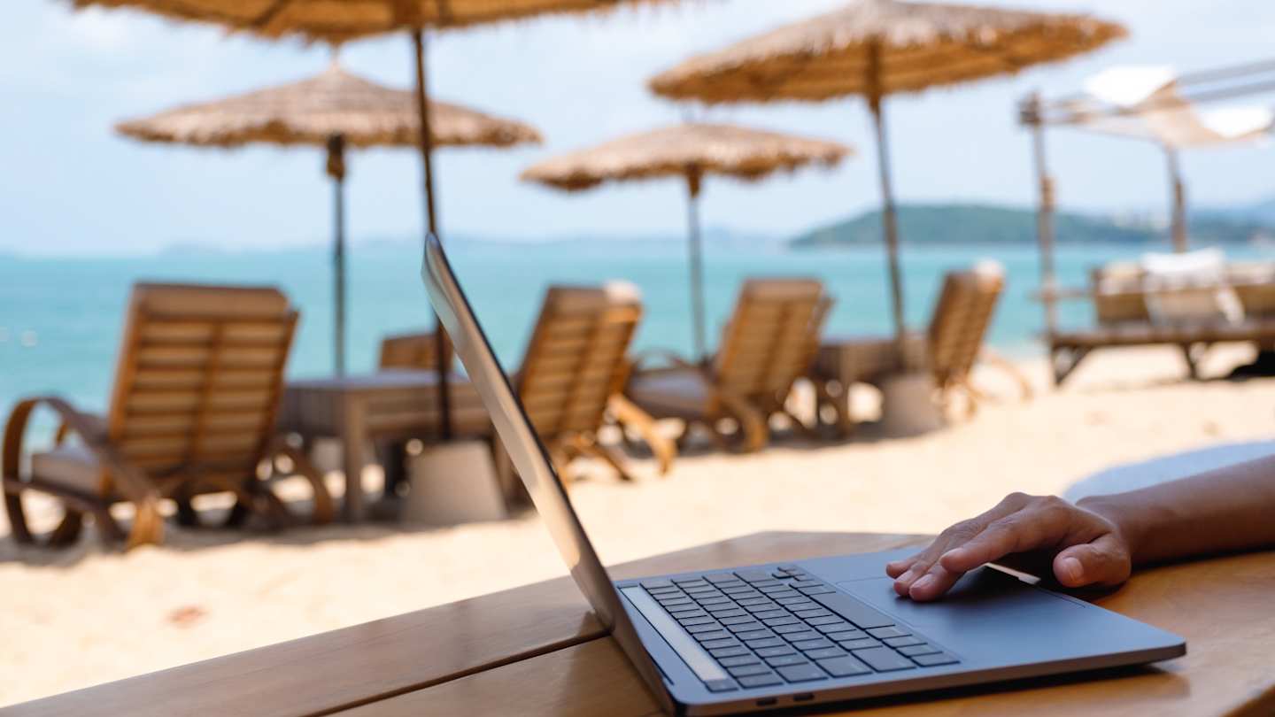 A close up of a digital nomad using a laptop at a beach in Europe