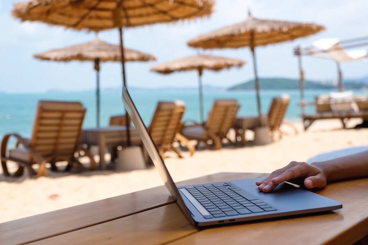 A close up of a digital nomad using a laptop at a beach in Europe