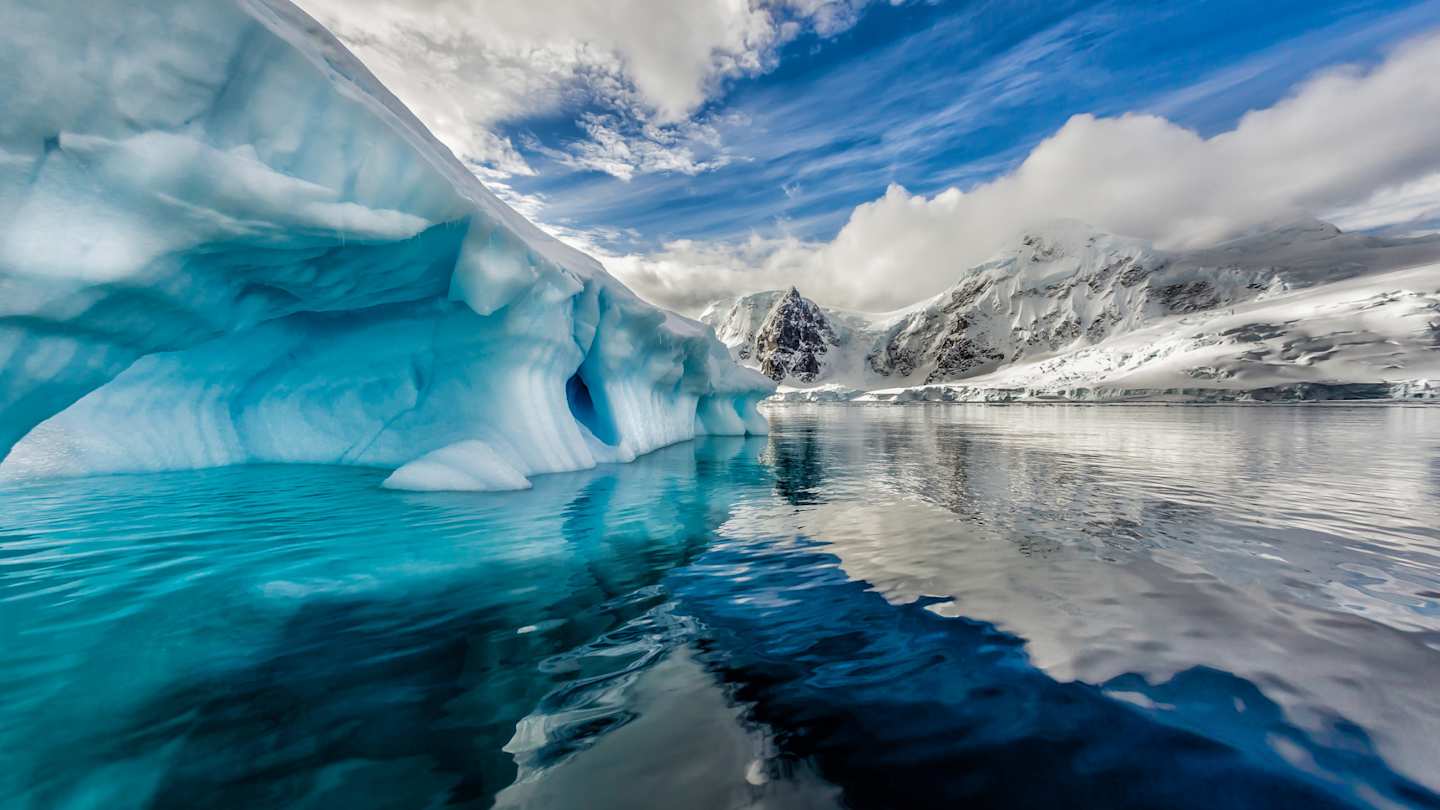 A view of tall icebergs and clear water in front of snow-capped mountains, Antarctica