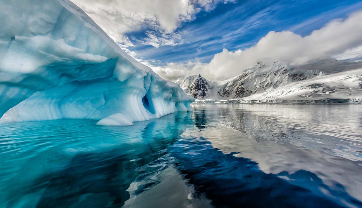 A view of tall icebergs and clear water in front of snow-capped mountains, Antarctica