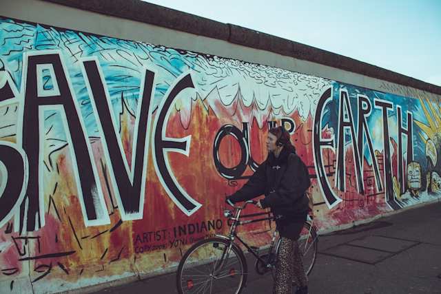 man walking with his bicycle near save our earth painted wall during daytime