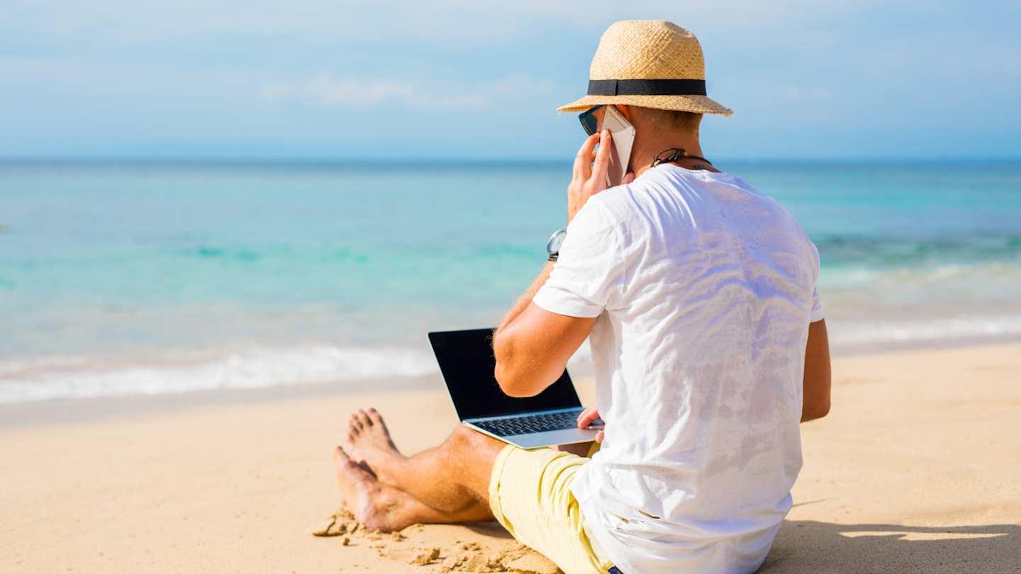 A man working on the beach with his laptop while taking a phone call