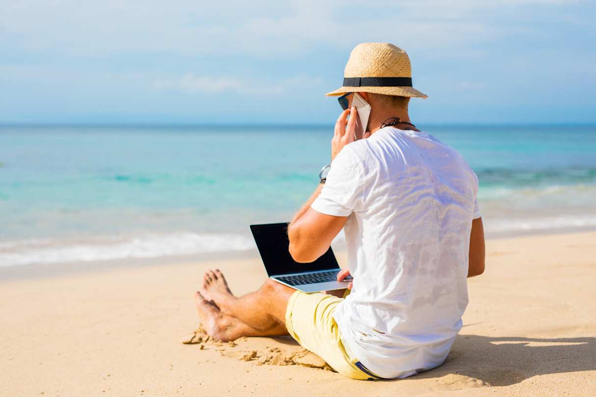 A man working on the beach with his laptop while taking a phone call