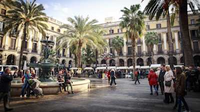 People among palm trees, buildings and a water fountain in a typical square in Barcelona, Spain