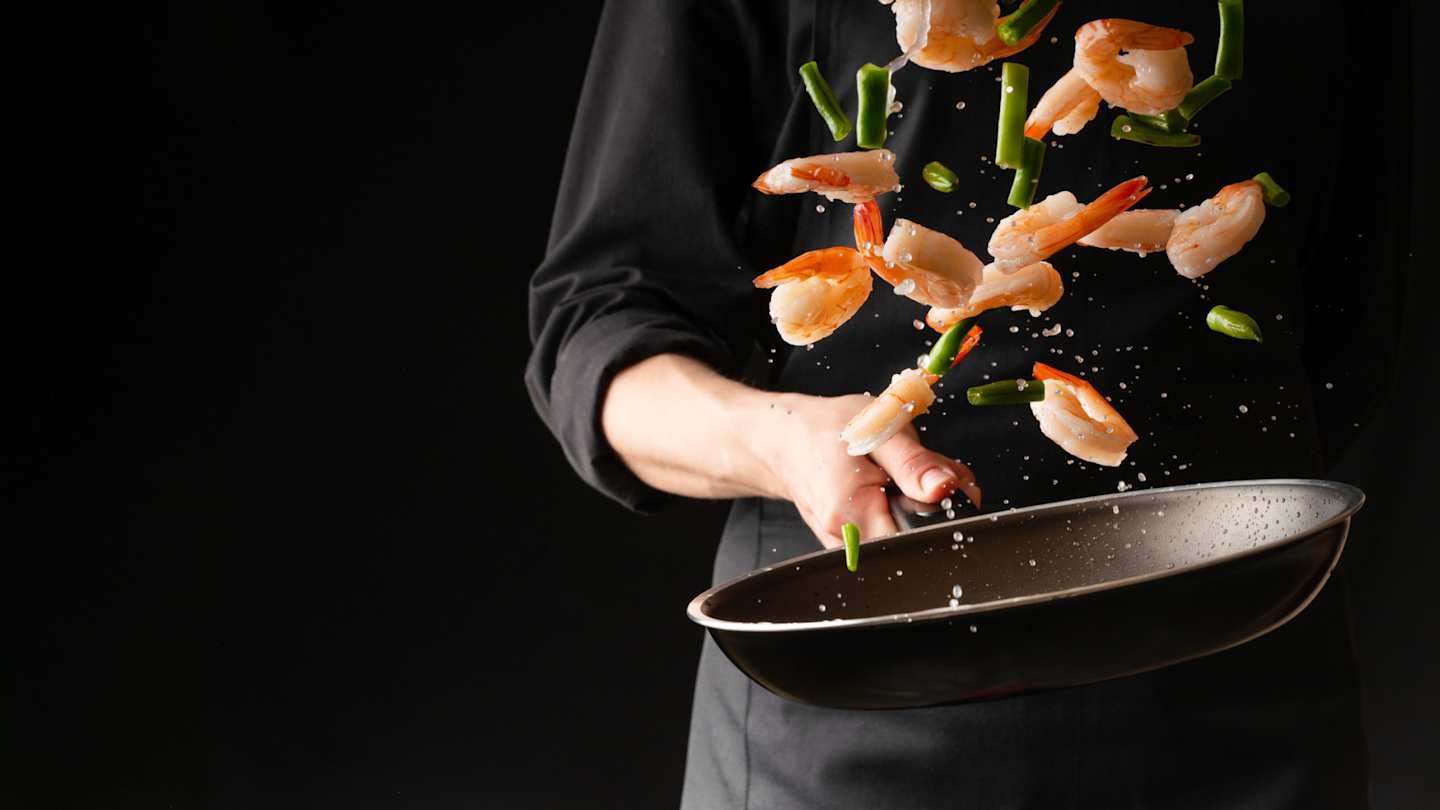 A professional chef tossing seafood in a saucepan