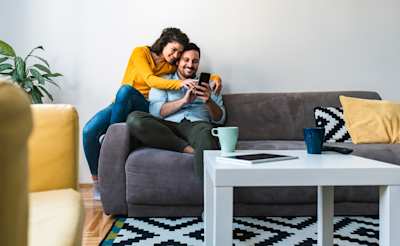 A host couple sitting on a sofa, smiling while looking at a mobile phone
